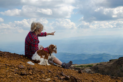 Woman with dog sitting on mountain against sky
