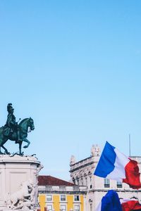 Low angle view of statue against buildings against clear blue sky