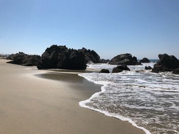 Rocks on beach against clear blue sky