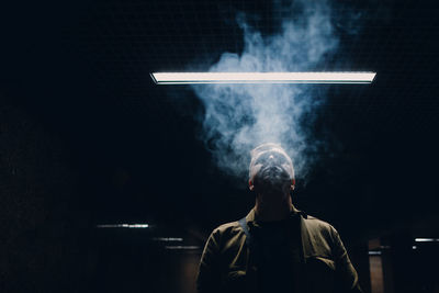 Man smoking while standing against black background