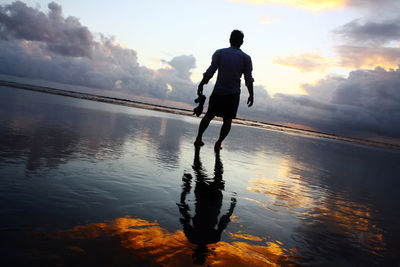 Tilt shot of silhouette man standing on shore at beach against sky