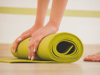 Low section of woman folding exercise mat on hardwood floor