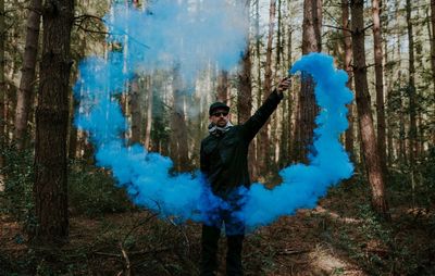 Young man holding distress flare while standing in forest