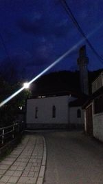 Illuminated street amidst buildings against sky at night