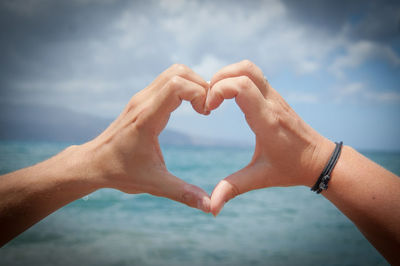 Midsection of woman making heart shape against sky