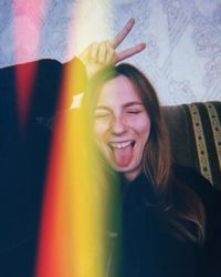 Close-up of smiling young woman gesturing peace sign while sticking out tongue