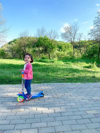 Full length side view of cute girl standing on push scooter at footpath