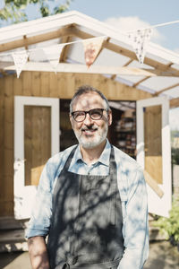 Portrait of happy mature store owner standing against shop