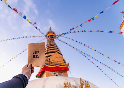 Low angle view of hand holding paper with text against temple building and sky