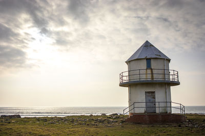 Lighthouse on beach against sky during sunset