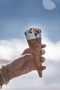 Person holding ice cream cone against sky
