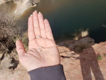 Cropped hand of person holding rock over lake