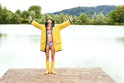 Woman wearing raincoat while standing on pier over lake during rainy season