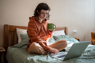 Clever diligent concentrated schoolgirl sitting on bed, studying at home using laptop computer