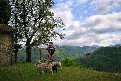 Young man standing with dogs on grassy mountain against sky