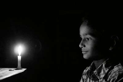 Close-up of boy with candle against black background