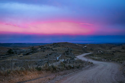 Dirt road amidst landscape against sky during sunset