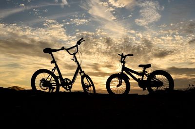 Silhouette bicycles on field against sky during sunset