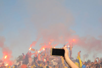 Cropped hand photographing people against sky