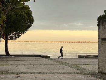 Man standing by lake against sky during sunset