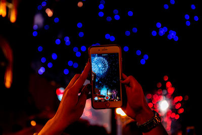 Man photographing illuminated mobile phone at night