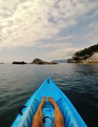 Low section of person relaxing in kayak against cloudy sky