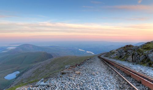 Railroad track amidst mountains against sky during sunset