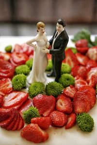 Fresh strawberries over wedding cake with pregnant bride and groom figurine. 