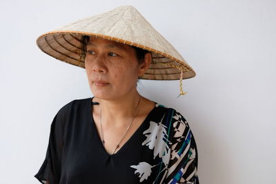 Close-up of mature woman wearing asian style conical hat against wall