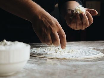 Midsection of man preparing pizza at table in home