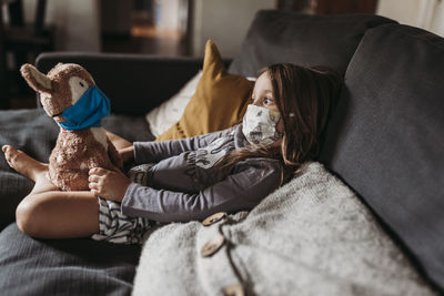 Preschool age girl with mask on cuddling stuffed animal with mask