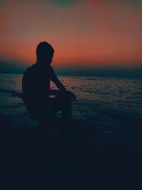 Rear view of man standing on beach against sky during sunset