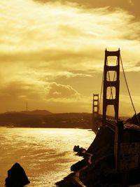 Silhouette bridge over sea against sky during sunset