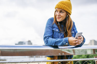 Smiling young woman wearing yellow cap listening music with earphones