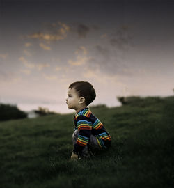 Boy looking away on field against sky during sunset