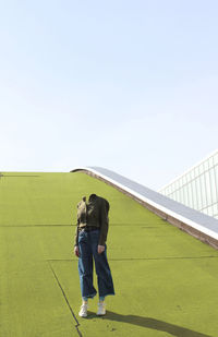 Rear view of man and woman standing on grass against sky