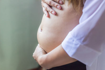 Midsection of pregnant woman making heart shape on stomach 