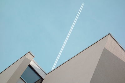 Low angle view of vapor trail over building against clear blue sky