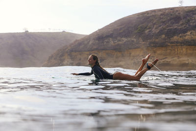 Happy woman sitting on surfboard in sea