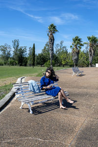 Rear view of woman sitting on field against sky