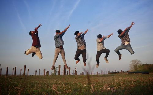 Group of people jumping on field against sky