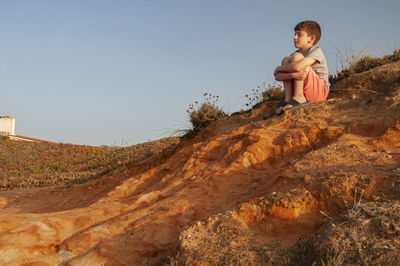 Kid or child meditates with closed eyes on a rocky coast during sunset. 