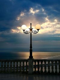 Street light by sea against sky during sunset