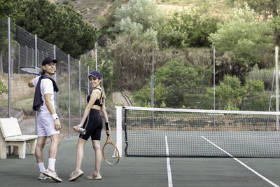 Back view of couple walking on tennis court looking to camera having fun and smiling with copy space