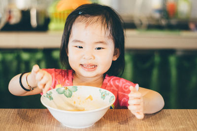 High angle view of smiling girl eating food while sitting by table at home