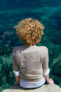 Rear view of woman sitting on rock against sea