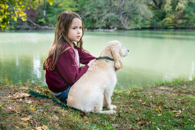 Girl sitting with english cocker spaniel on the river bank. kid walking dog in forest . 