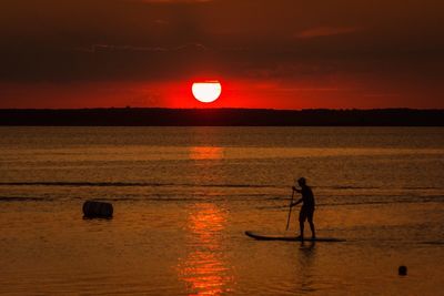 Man paddleboarding in sea against sky during sunset