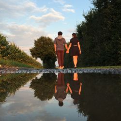 Rear view of men standing by lake against sky