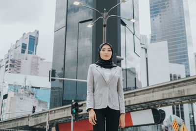 Portrait of woman standing against buildings in city